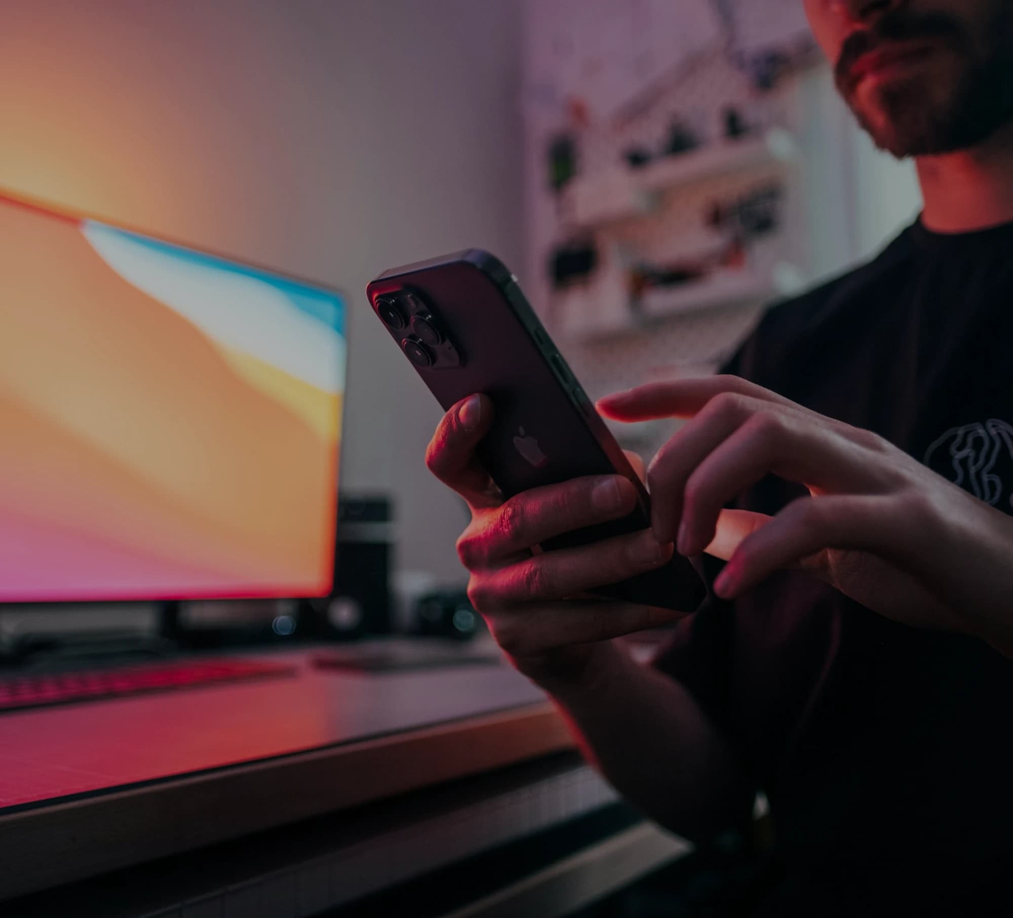 Someone using a phone at a desk in front of a monitor